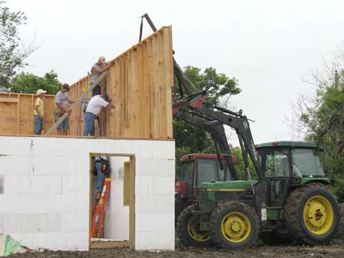 Using a boom on a tractor to lower walls into place.