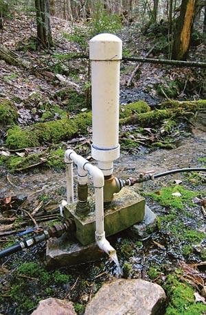 My Atlas Ram Pump; intake on left, delivery pipe on right. The large white pipe is the pressure chamber; to the left of it is a diverter for the waste water.